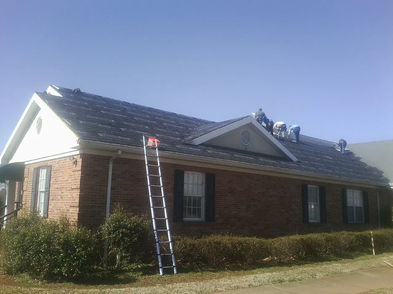 Crew tearing shingles off a brick ranch roof with a ladder set — Metal Roof Repair work by our crew in Walhonding