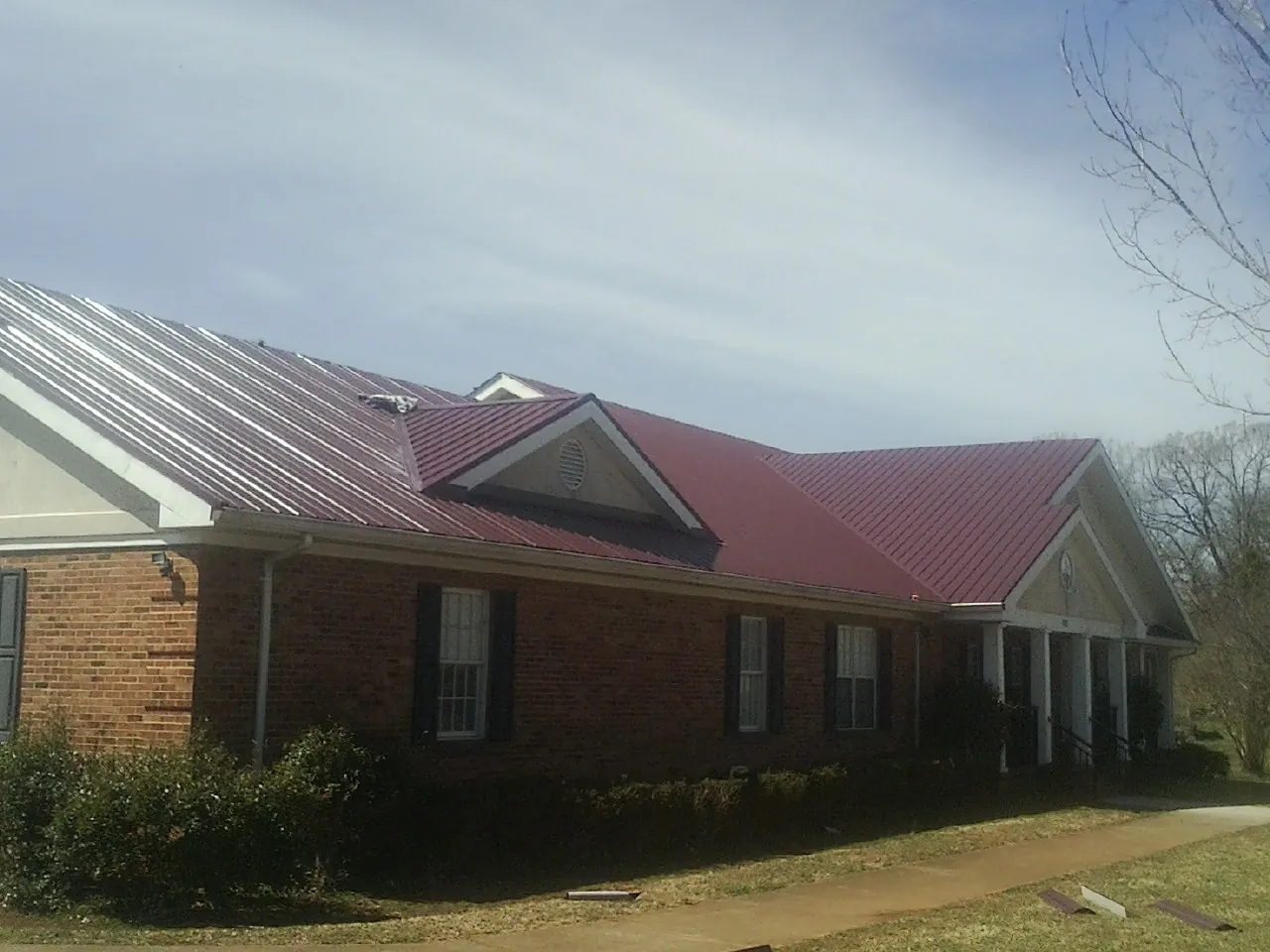 Red metal roof with gabled entries on a long brick building, from a Hail Damage Roof Repair job in Walhonding