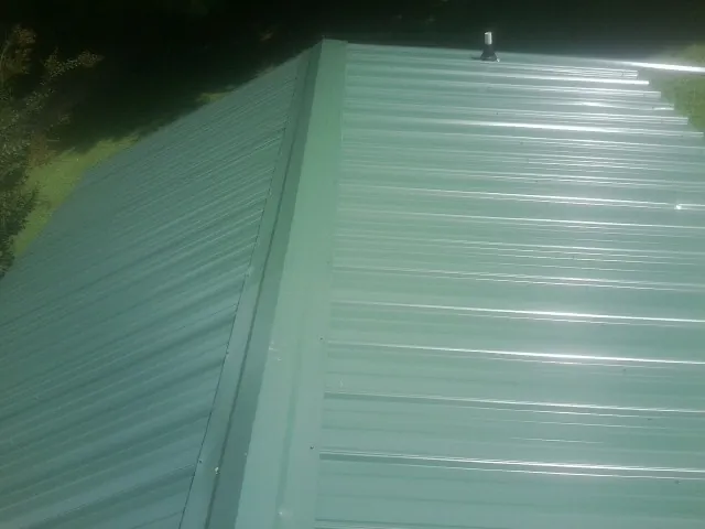New green metal panels meeting at the ridge of a roof — Flat Roof Repair work by our crew in Walhonding